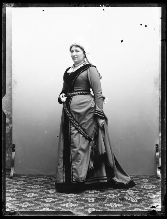 Studioaufnahme. Porträt einer stehenden Frau im Kleid mit Schlüsselbund und Kopftuch