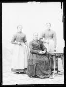 Ripresa in studio. Ritratto di gruppo di due donne in piedi e una seduta. A sinistra c'è un  tavolo