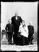 Ripresa di studio. Ritratto di gruppo: un uomo, una donna, due ragazzini e una bambina, la quale è seduta sulle gambe della donna. Vicino di loro un tavolo