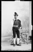 Studioaufnahme. Ritratto di un uomo in piedi con cappello, baffi, pipa e costume regionale.