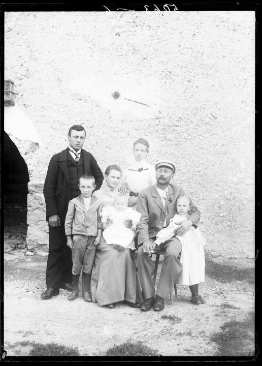 Außenaufnahme. Gruppenporträt von zwei Frauen, zwei Männern und drei Kindern im Freien, dahinter ein Steinbogen