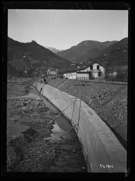Außenaufnahme. Baustelle mit Arbeitern. Bau der Wassermauer in Bozen. Gebäude mit der Aufschrift