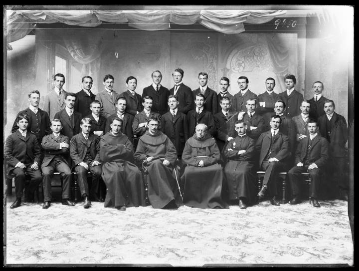 Studioaufnahme. Gruppenporträt von 33 Männern, in der Mitte vier Geistliche sitzend