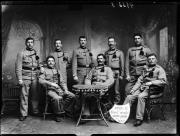 Ripresa in studio. Ritratto di gruppo, otto soldati in uniforme. In mezzo c'è un tavolo e vicino uno scudo con l'iscrizione 