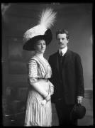 Ripresa in studio. Ritratto di gruppo, una donna e un uomo. Lei porta un cappello con piume. Lui tiene un cappello nella mano