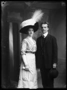 Ripresa in studio. Ritratto di gruppo, una donna e un uomo. Lei porta un cappello con piume. Lui tiene un cappello nella mano