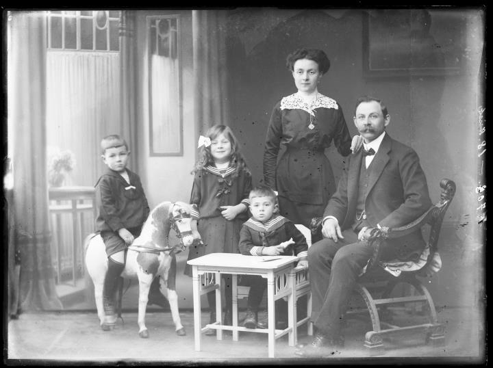 Studioaufnahme. Gruppenporträt: ein Mann, eine Frau und drei Kinder, eines davon sitzt auf einem Schaukelpferd. Information im Register (Nr. 22): 