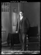 Ripresa in studio. Ritratto di un uomo in piedi davanti a un tavolo e una sedia. Informazione nel registro: Burger Josef