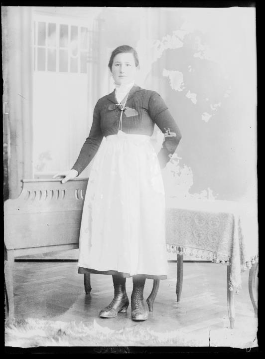 Studioaufnahme. Porträt einer stehenden Frau mit Bank und Tisch. Information im Register (Nr. 4): Gasser Luise, Schletscher