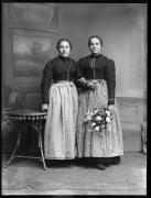 Ripresa in studio. Ritratto di gruppo di due donne in piedi in costume regionale. Una tiene un mazzo di fiori in mano