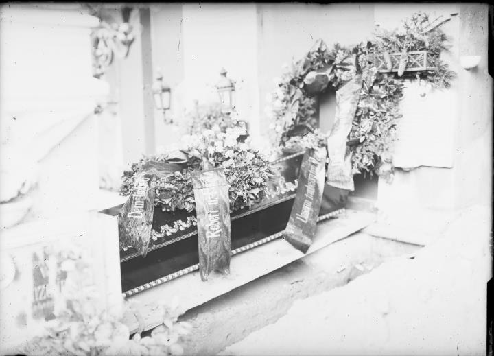Außenaufnahme. Friedhof. Sarg neben offenem Grab mit Blumenkränzen mit Bändern mit der Aufschrift 