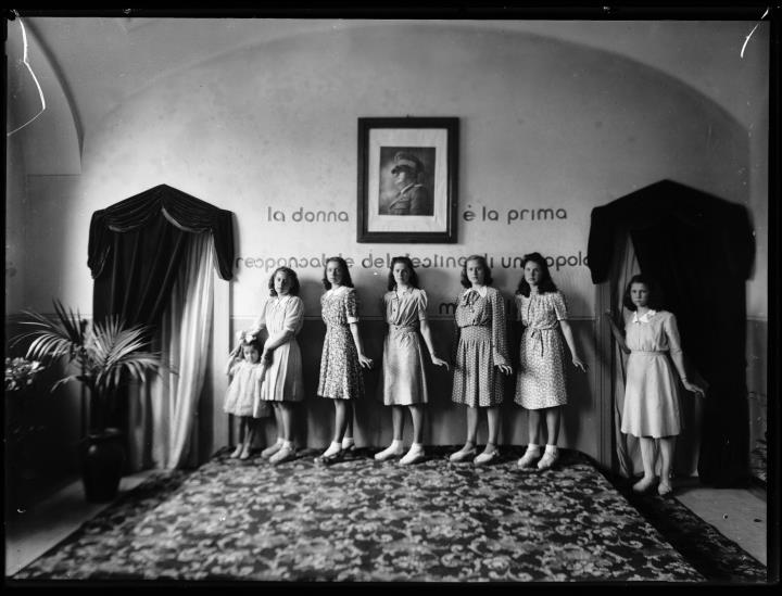 Innenaufnahme. Gruppenporträt von sieben Frauen und einem Kind . Auf der Wand die Aufschrift: 