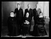 Ripresa interno. Ritratto di gruppo di tre uomini e tre donne. La donna al centro ha un mazzo di fiori e due donne sono suore